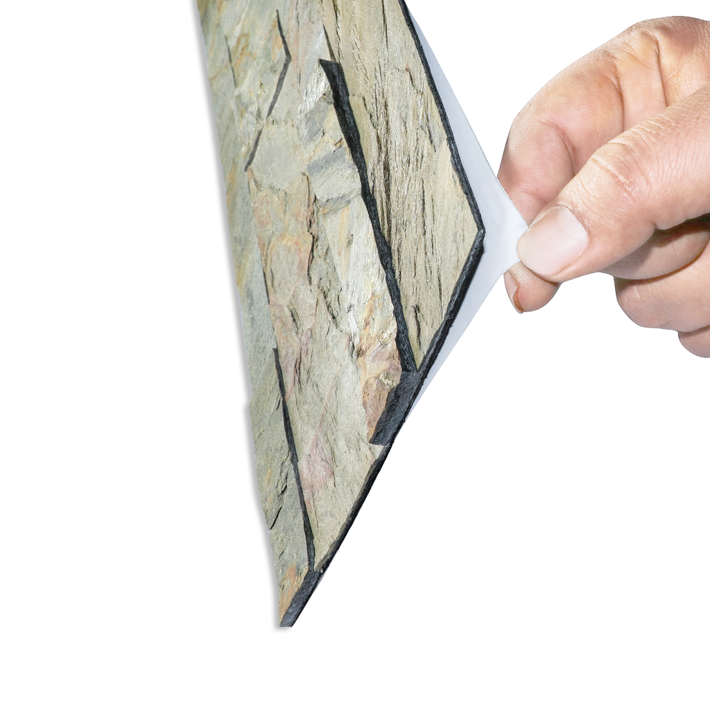 A product image of green & grey colored burning forest peel and stick self-adhesive real stone wall tiles from stoneflex shown sideways with a hand peeling the protective film off its self-adhesive back.