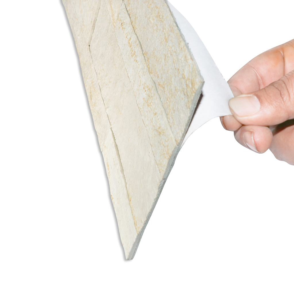 A product image of off-white colored ecru white peel and stick self-adhesive real stone wall tiles from stoneflex shown sideways with a hand peeling the protective film off its self-adhesive back.